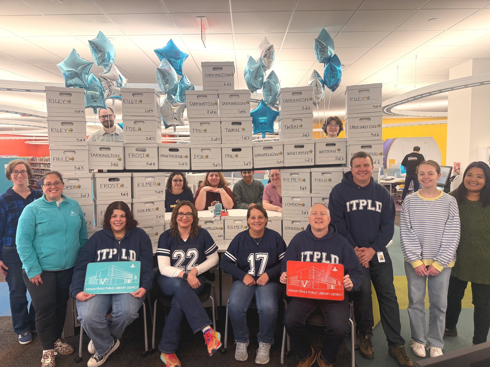 Staff members involved in the CCSD21 library card initiative surround the fortress of boxes filled with student library card packets.