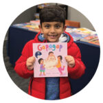 A boy holds up a Hindi book called "Gapagap"
