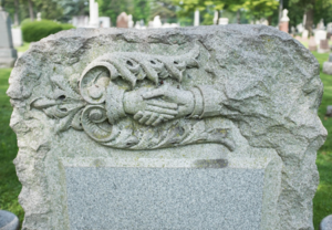 A gravestone with a handshake engraved in the stone.